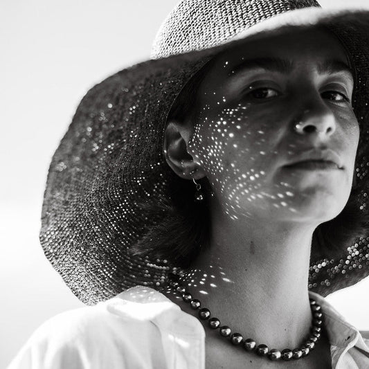 Black and white photo of a person wearing a wide-brimmed hat with sunlight filtering through.
