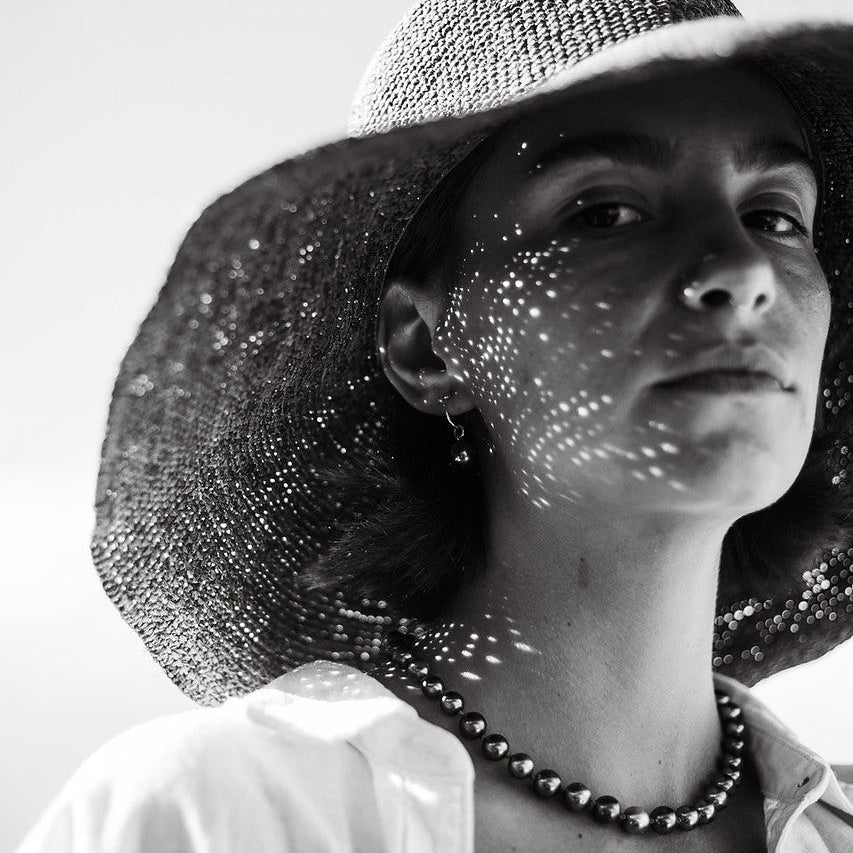 Black and white photo of a person wearing a wide-brimmed hat with sunlight filtering through.
