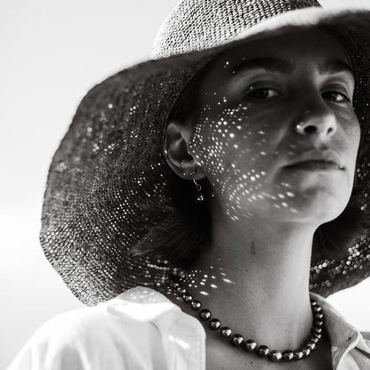 Black and white photo of a person wearing a wide-brimmed hat with sunlight filtering through.