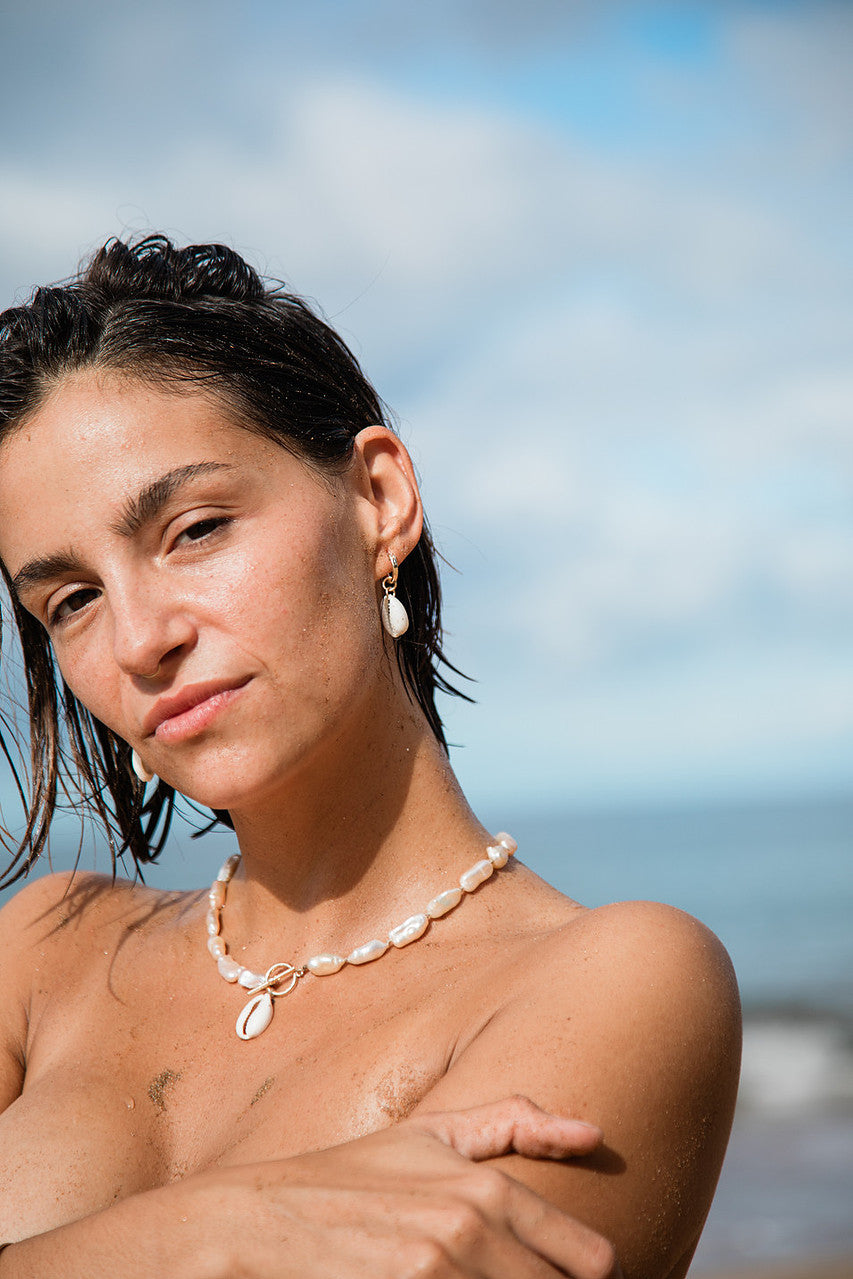 Woman with wet hair and a necklace standing against a blurred beach background