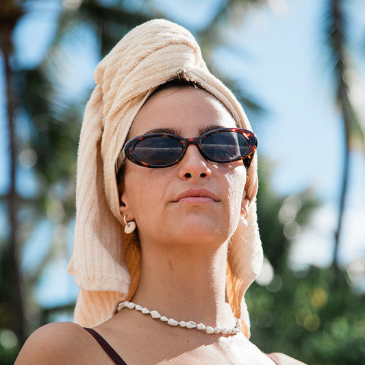Woman wearing sunglasses and a towel on her head outdoors with palm trees in the background