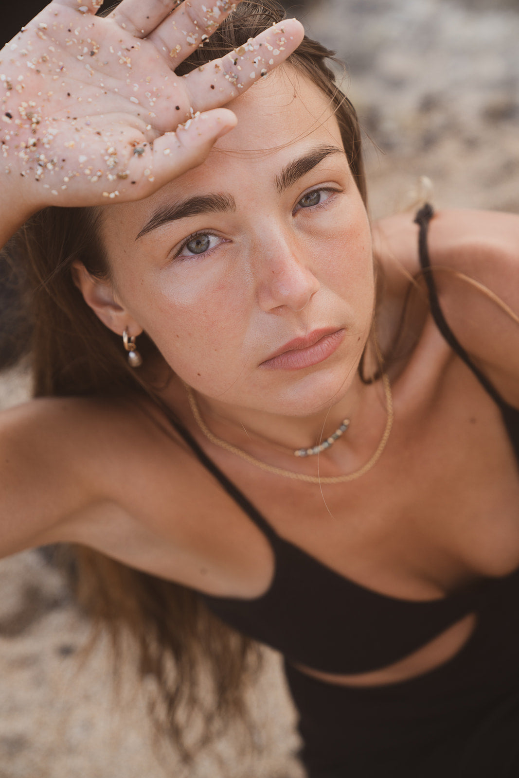 Close-up of woman wearing Studio Immersed necklace and earrings with sand on skin