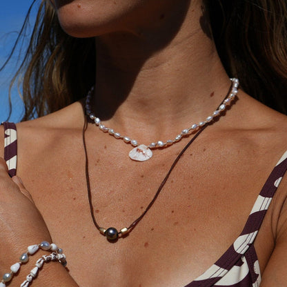 Clara wearing our freshwater pearl strand with a beautiful and unique shell charm in the center. Layered with a pear l with gold beads on a leather string.